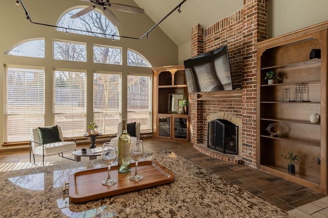 living area with high vaulted ceiling, a brick fireplace, ceiling fan, and wood finished floors