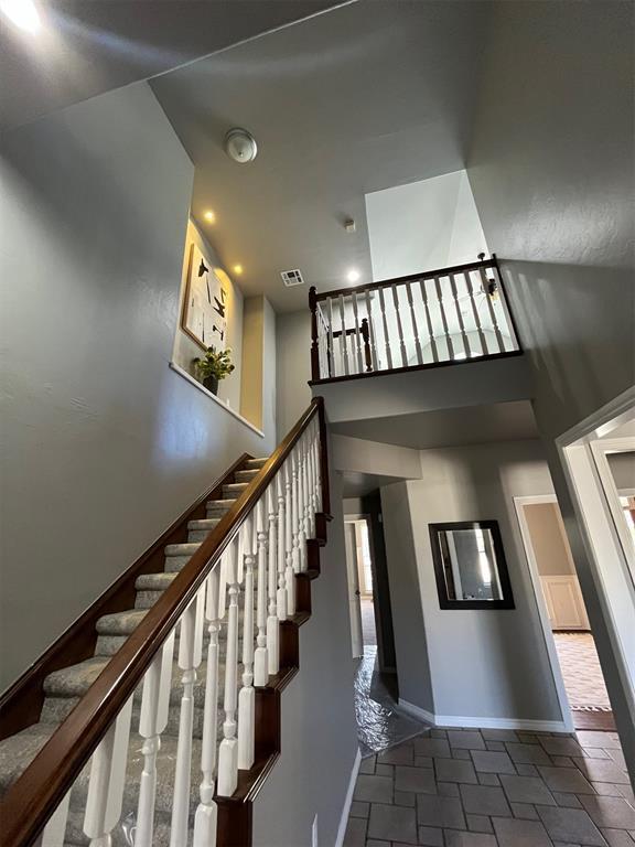 stairway with stone tile flooring, baseboards, visible vents, and a high ceiling