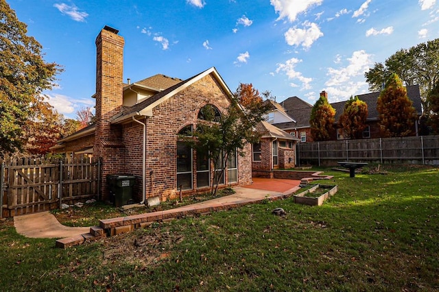 rear view of house with brick siding, a chimney, a fenced backyard, and a lawn