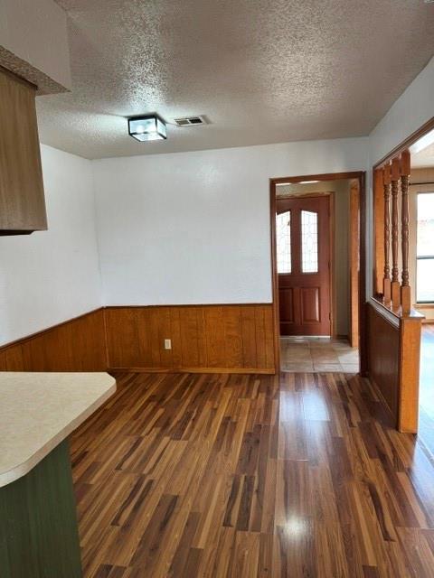 entrance foyer featuring a wainscoted wall, dark wood finished floors, visible vents, wooden walls, and a textured ceiling