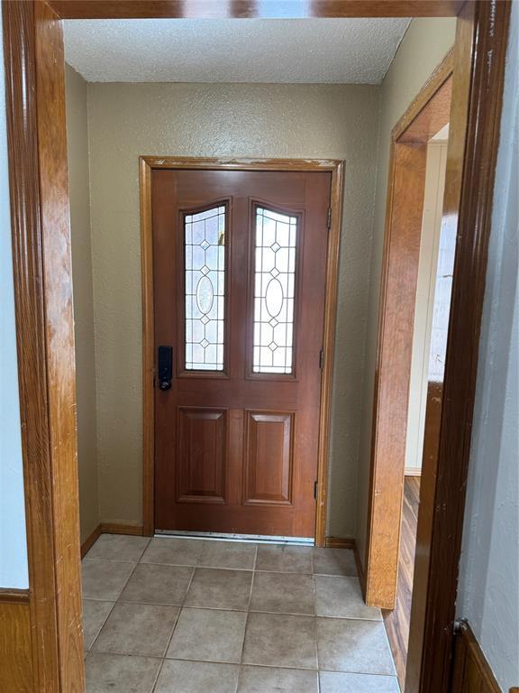 entrance foyer featuring light tile patterned floors, baseboards, and a textured wall