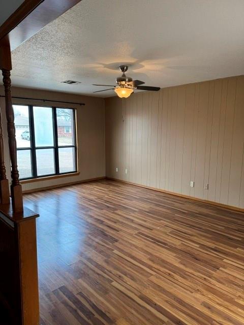 spare room featuring a textured ceiling, wood finished floors, visible vents, baseboards, and a ceiling fan