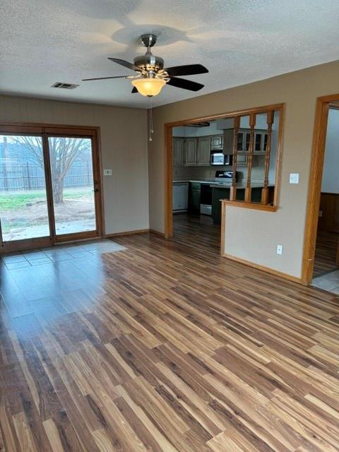 unfurnished living room with a textured ceiling, wood finished floors, visible vents, baseboards, and a ceiling fan