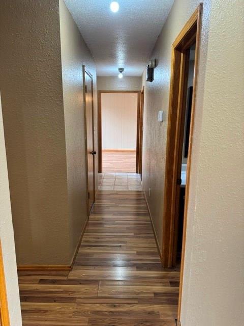 hallway featuring dark wood-style floors, baseboards, and a textured wall