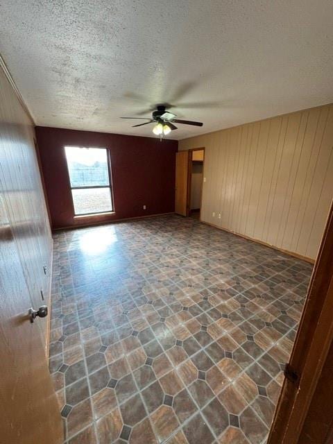 unfurnished room featuring a ceiling fan, wood walls, and a textured ceiling