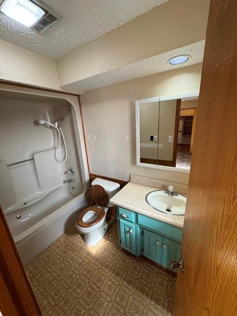 full bath featuring visible vents, toilet, a textured ceiling, vanity, and washtub / shower combination