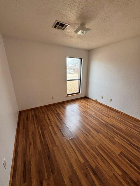 empty room featuring a textured ceiling, visible vents, and dark wood-type flooring