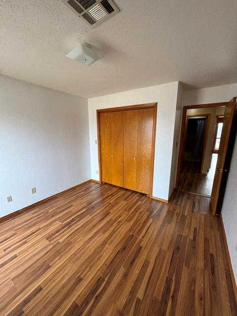 unfurnished bedroom with a closet, visible vents, dark wood-type flooring, a textured ceiling, and baseboards