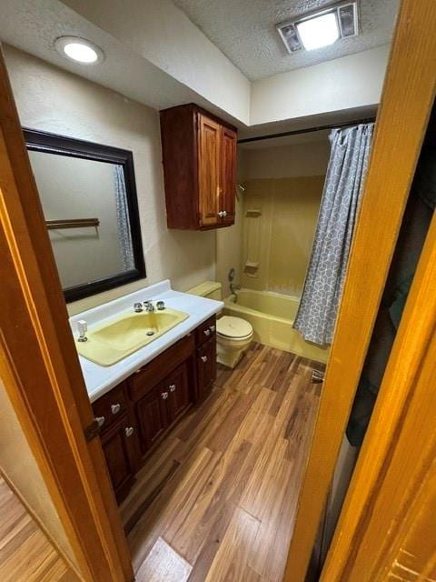 full bathroom with toilet, shower / tub combo with curtain, wood finished floors, a textured ceiling, and vanity