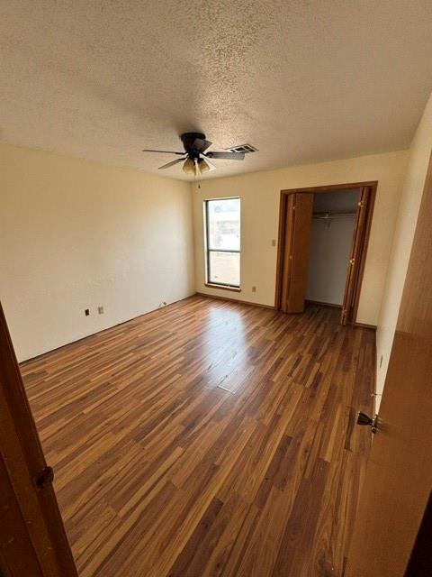 unfurnished bedroom with dark wood-style flooring, a closet, visible vents, a ceiling fan, and a textured ceiling