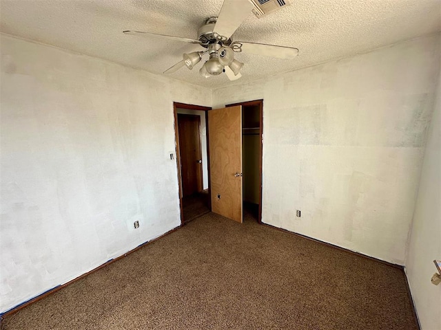 unfurnished bedroom with a textured ceiling, ceiling fan, visible vents, a closet, and dark carpet