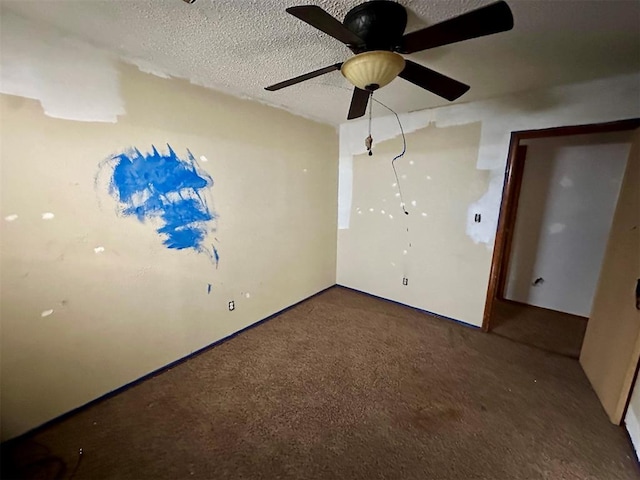 empty room featuring a ceiling fan, dark carpet, and a textured ceiling