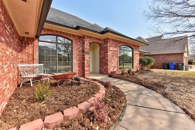 view of exterior entry with brick siding, a shingled roof, and visible vents