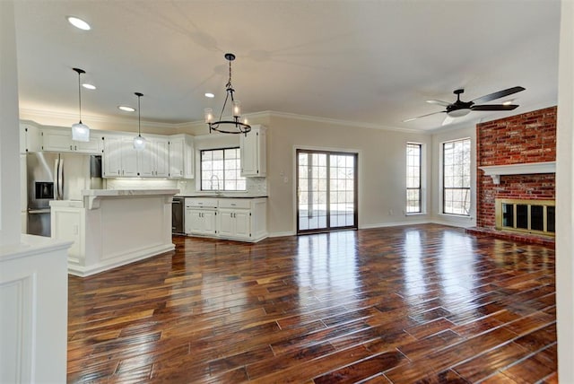 unfurnished living room with dark wood finished floors, crown molding, a brick fireplace, a sink, and ceiling fan with notable chandelier