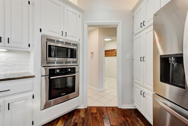 kitchen featuring white cabinets, dark wood finished floors, dark stone countertops, stainless steel appliances, and backsplash