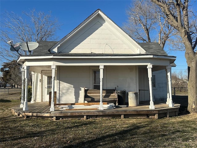 rear view of property featuring a porch, a lawn, and roof with shingles