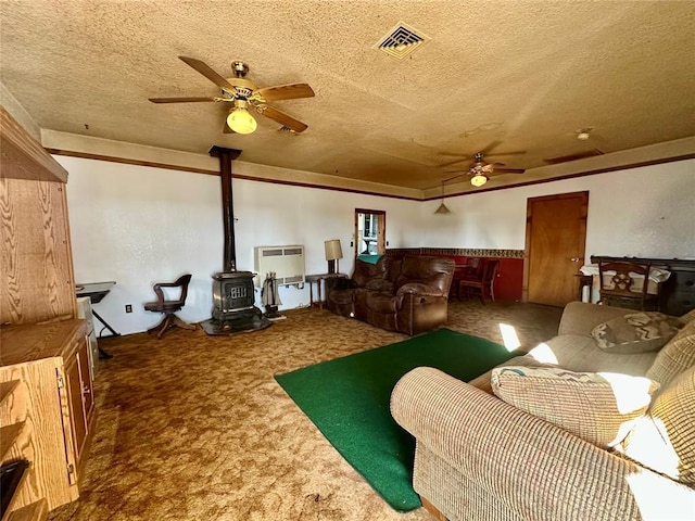 carpeted living area featuring ceiling fan, visible vents, a textured ceiling, and a wood stove