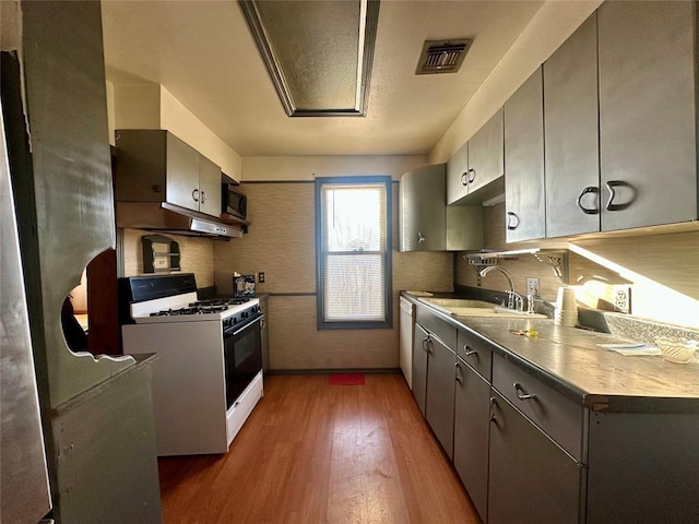 kitchen featuring dark wood-style flooring, a sink, backsplash, stainless steel microwave, and white gas range