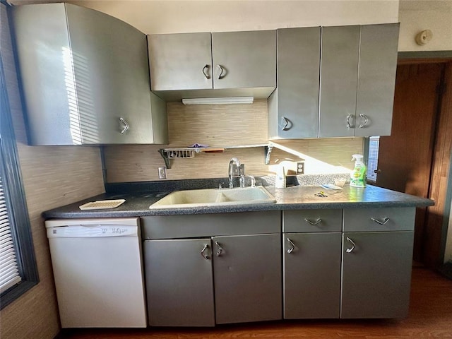 kitchen with dishwasher, dark countertops, backsplash, gray cabinetry, and a sink