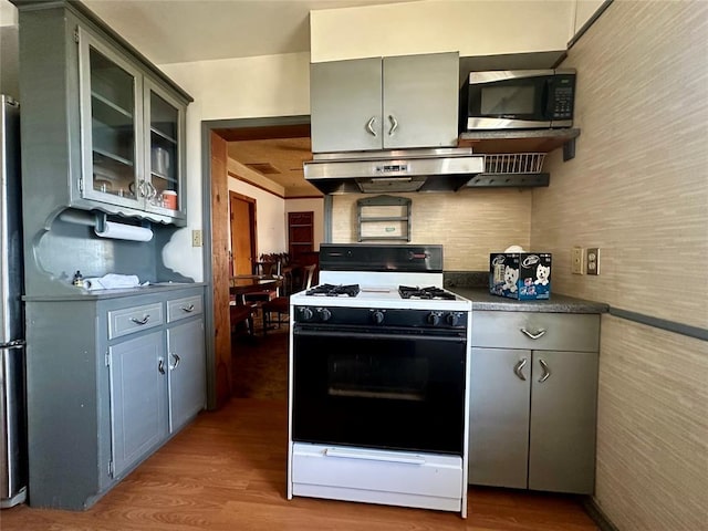 kitchen with gas range oven, dark countertops, gray cabinets, stainless steel microwave, and under cabinet range hood