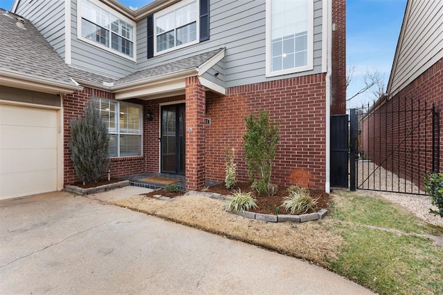 view of exterior entry with a garage, brick siding, a shingled roof, and fence