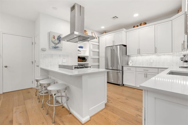 kitchen with visible vents, white cabinets, freestanding refrigerator, island exhaust hood, and light countertops