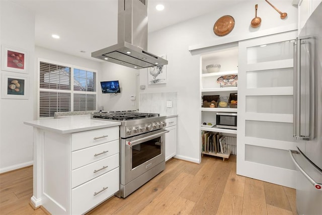 kitchen with island exhaust hood, light countertops, white cabinetry, high quality appliances, and light wood-type flooring