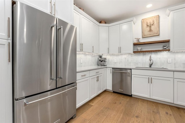 kitchen with white cabinets, appliances with stainless steel finishes, light countertops, light wood-type flooring, and a sink