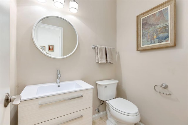 half bath featuring baseboards, vanity, and toilet