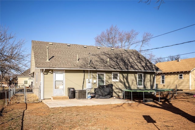 rear view of property with a patio, a shingled roof, fence, a gate, and a trampoline