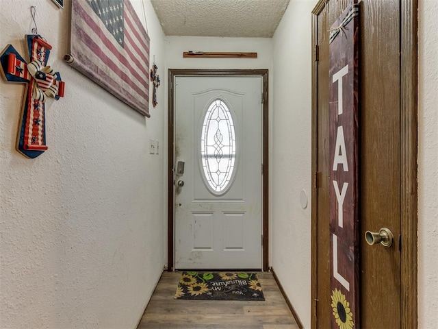 doorway to outside with light wood-style flooring, a textured ceiling, and a textured wall