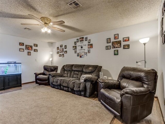 living room with ceiling fan, a textured ceiling, visible vents, and light wood-style floors