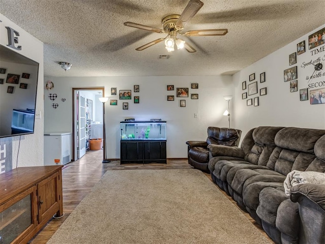 living room featuring ceiling fan, a textured ceiling, wood finished floors, and visible vents