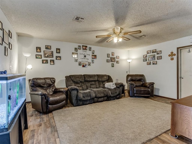 living area with a ceiling fan, visible vents, a textured ceiling, and wood finished floors