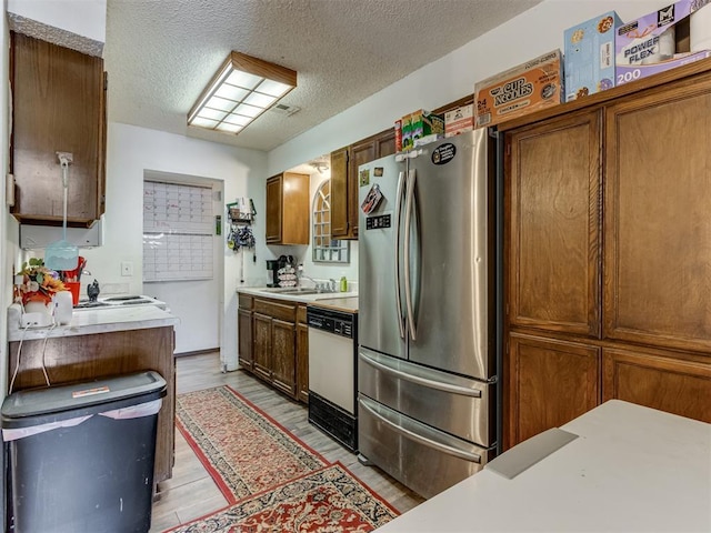 kitchen with brown cabinetry, light wood-style flooring, freestanding refrigerator, white dishwasher, and light countertops