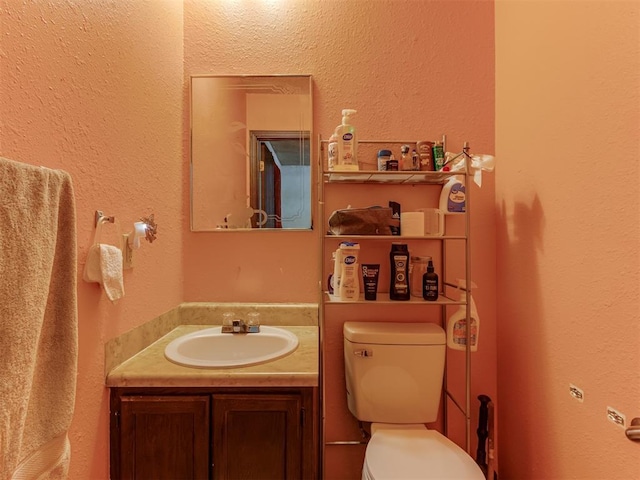 half bath with toilet, a textured wall, and vanity