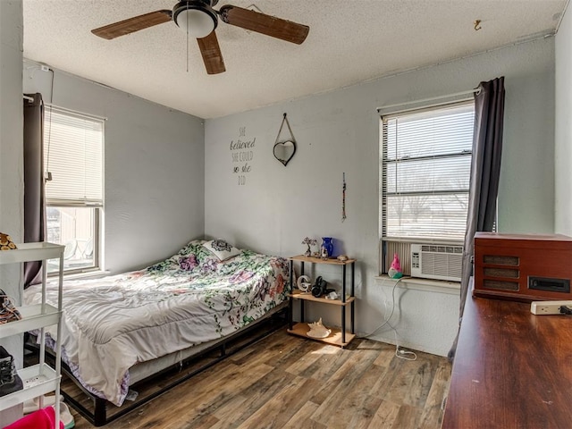 bedroom with ceiling fan, a textured ceiling, cooling unit, and wood finished floors