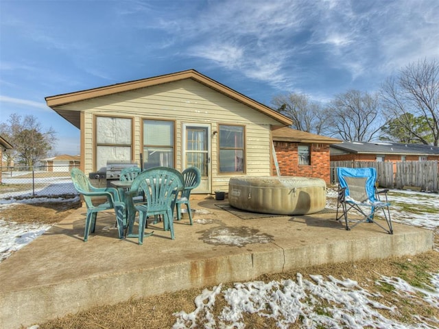 snow covered back of property featuring a patio, brick siding, fence, and a hot tub