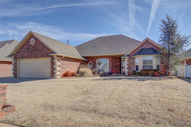 view of front facade with brick siding, a shingled roof, fence, a garage, and driveway