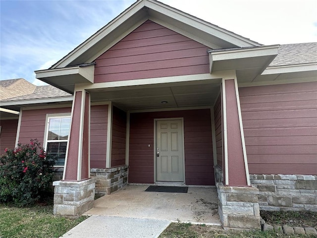 view of exterior entry featuring stone siding and a shingled roof