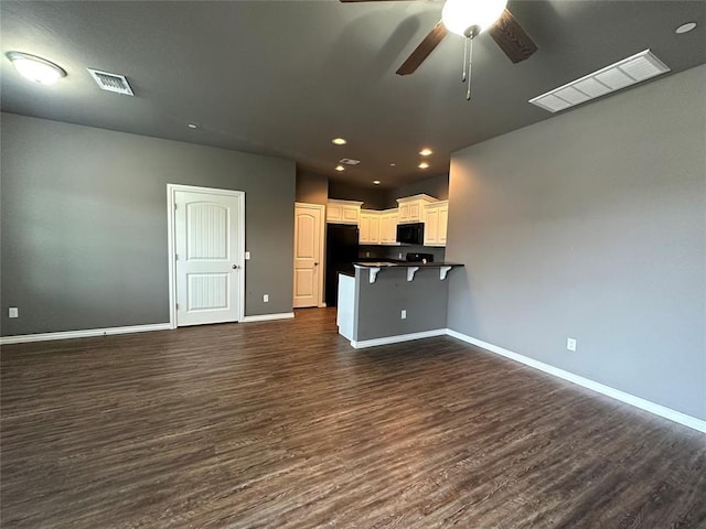 kitchen with a breakfast bar area, dark countertops, open floor plan, white cabinetry, and black appliances