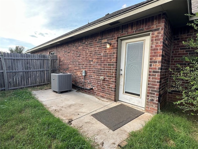 entrance to property with a patio, fence, cooling unit, and brick siding