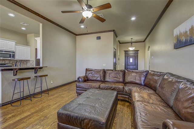 living area with light wood finished floors, arched walkways, crown molding, and recessed lighting