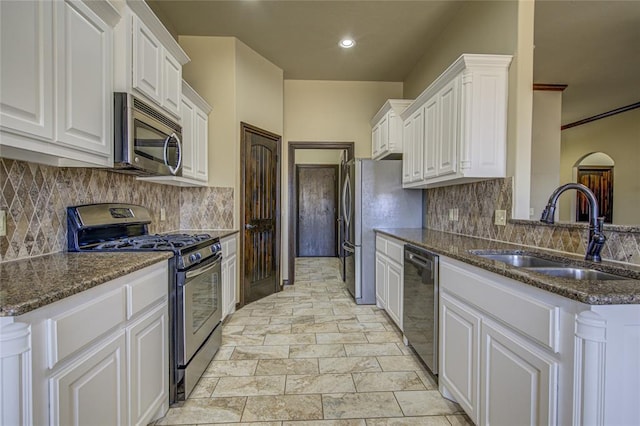 kitchen with appliances with stainless steel finishes, white cabinets, a sink, and dark stone countertops