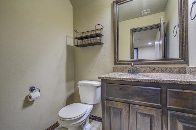 half bath featuring toilet, a textured wall, vanity, and visible vents