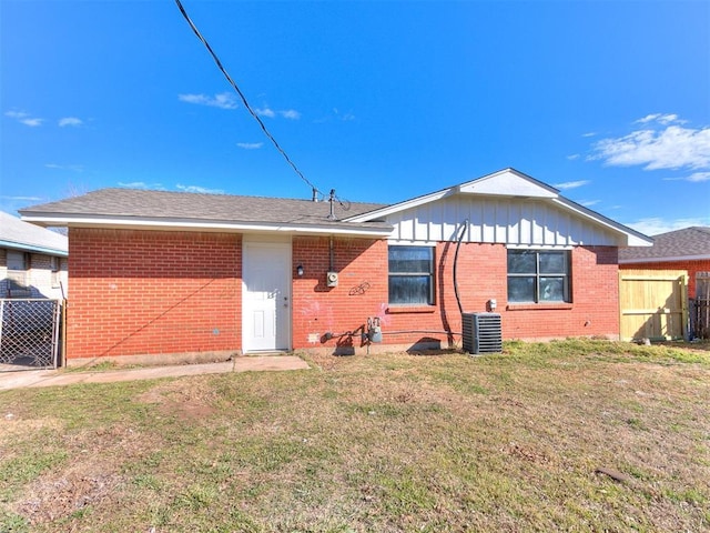 rear view of house featuring central air condition unit, brick siding, a lawn, and fence