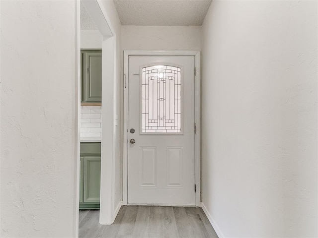 doorway featuring light wood-style floors, a textured ceiling, and a textured wall