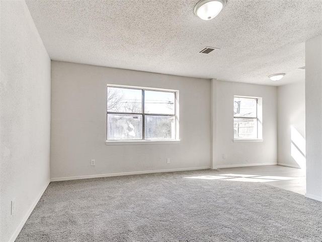 empty room featuring a textured ceiling, a textured wall, light carpet, visible vents, and baseboards