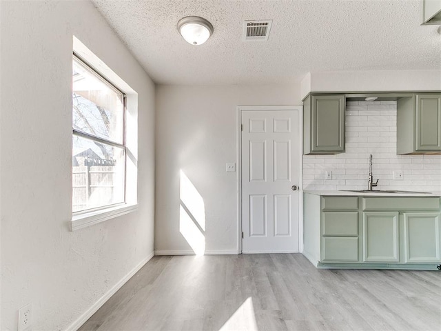 kitchen featuring a sink, visible vents, decorative backsplash, light wood finished floors, and green cabinetry