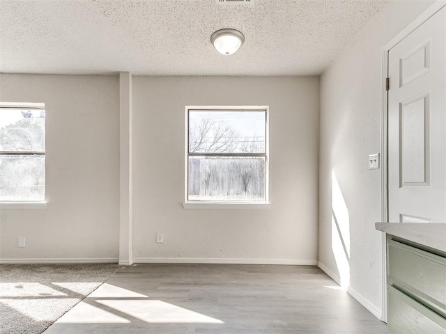 empty room featuring a textured ceiling, light wood-style flooring, and baseboards